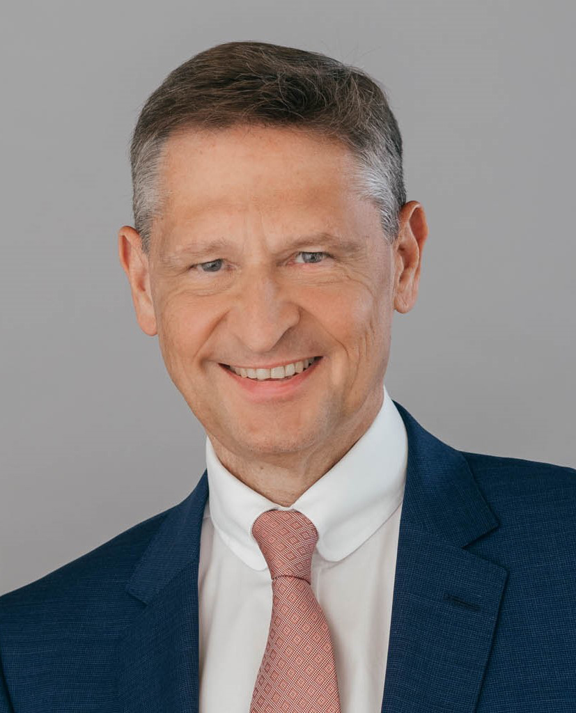 Porträt von Wolfgang Puff in dunkelblauem Anzug mit hellrosa Krawatte vor grauem Hintergrund.